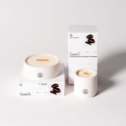 Fehér tégelyben és fehér dobozban elhelyezett Barista szójaviasz-gyertya – kávébab mintával és „MELT MY MOOD” felirattal –, világosszürke háttéren elrendezve.