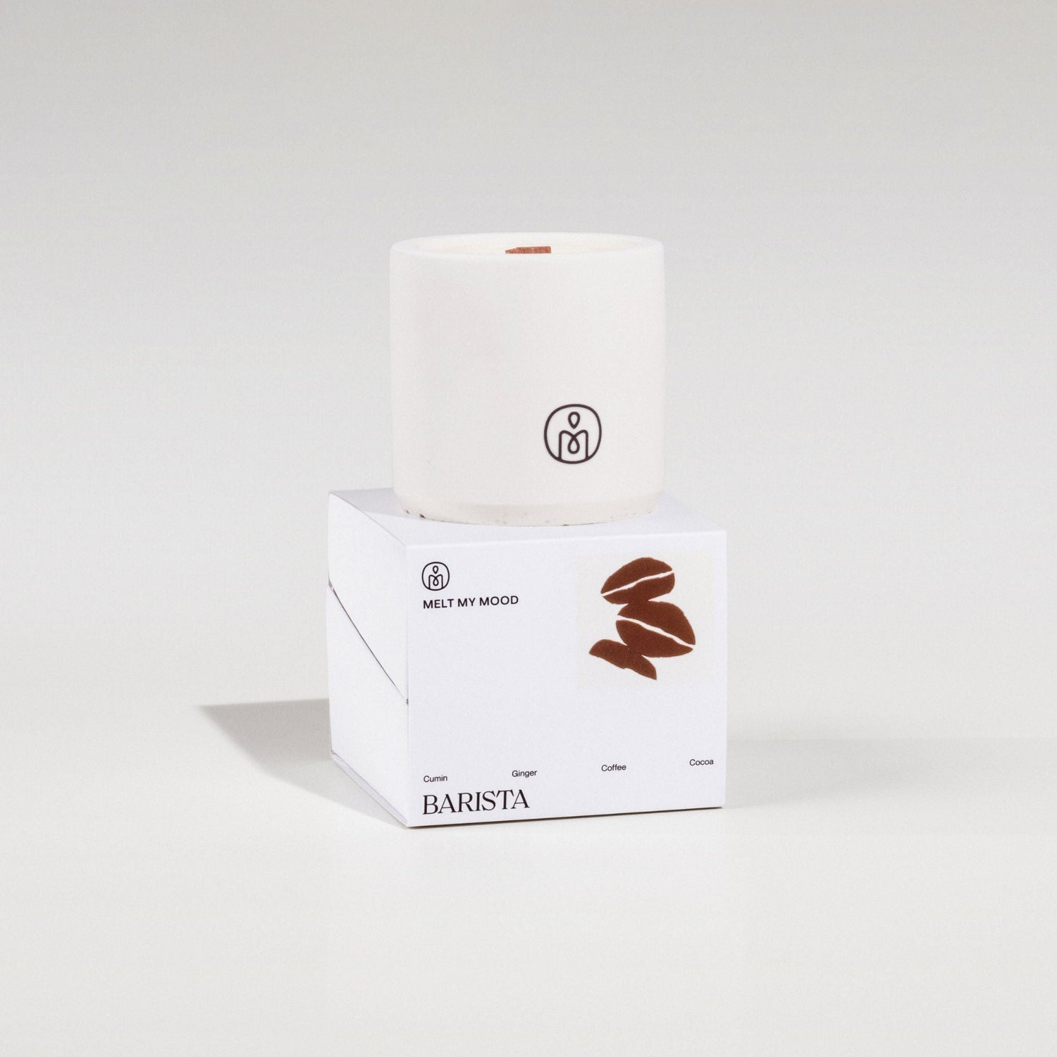 Egy henger alakú, törtfehér szójaviaszgyertya, benne fa kanóccal, egy fehér, kocka alakú dobozon áll. A dobozon a „BARISTA” (a gyertya neve) és egy barna kávészem ikon látható; a felvétel tiszta fehér stúdióháttér előtt, lágy árnyékkal készült.