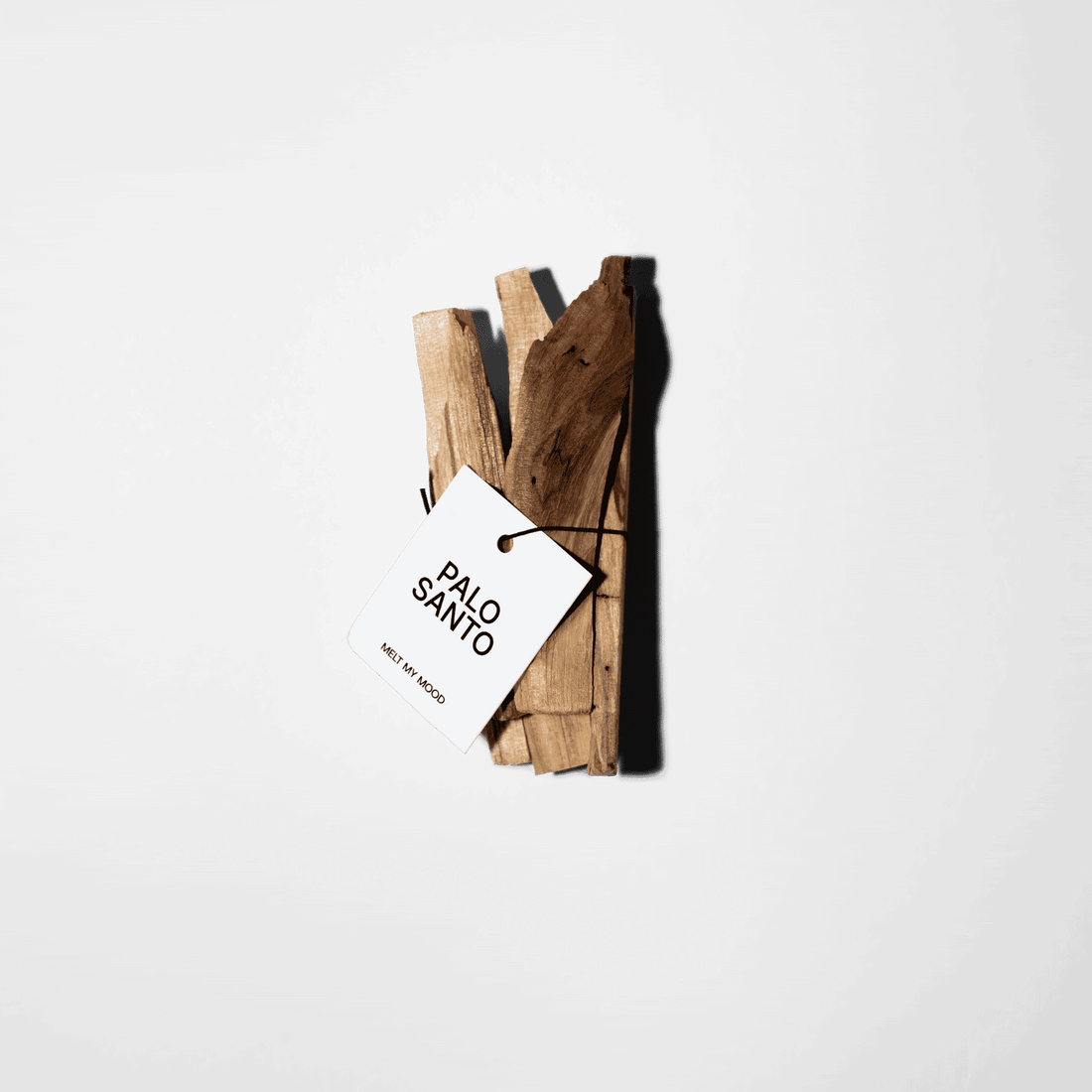Fekete zsineggel átkötött Palo Santo füstölőpálcika-köteg, amelyen egy fehér papírcédula látható a „PALO SANTO” és „MELT MY MOOD” felirattal; a kompozíció egyszínű fehér háttér előtt látható.