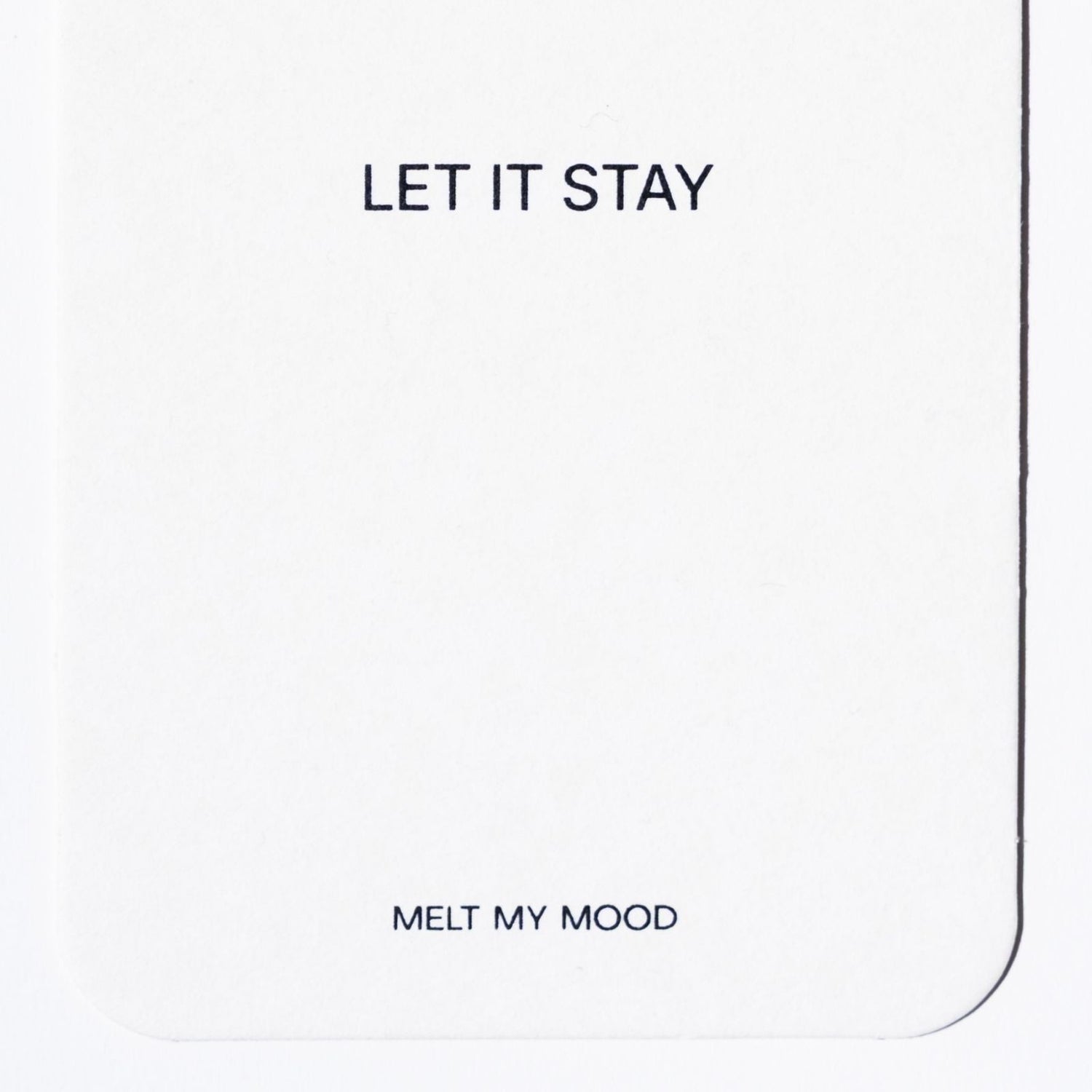 Közelkép egy lekerekített sarkú, fehér, téglalap alakú gardróbillatosítóról, amelynek felső részén a „LET IT STAY”, alsó részén pedig a „MELT MY MOOD” felirat látható fekete betűkkel.