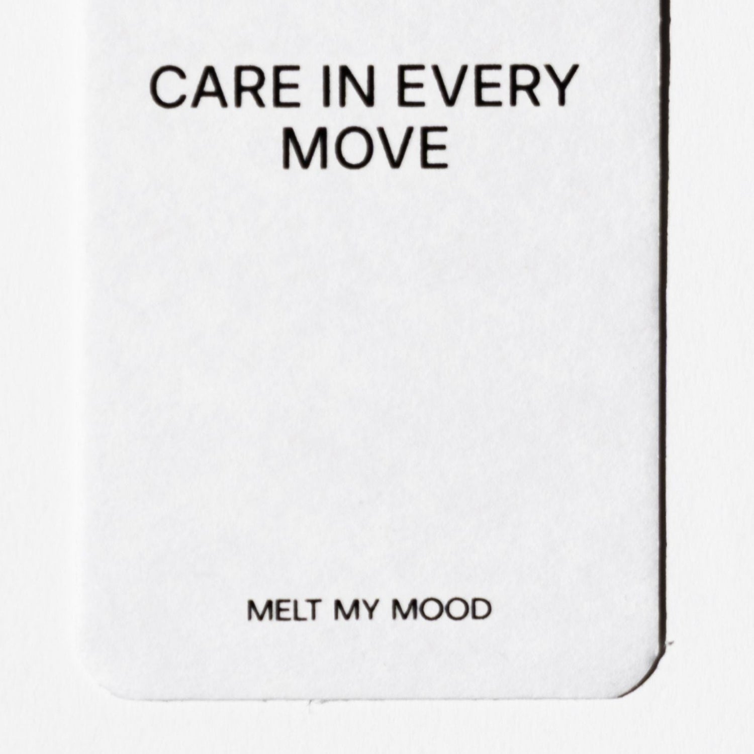 Lekerekített alsó sarkú, fehér, téglalap alakú autóillatosító; felső részén a „CARE IN EVERY MOVE”, alsó részéhez közel pedig a „MELT MY MOOD” felirat látható fekete betűkkel.