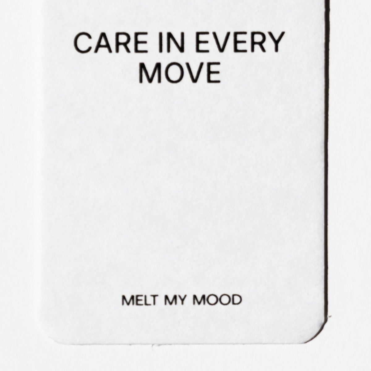 Lekerekített alsó sarkú, fehér, téglalap alakú autóillatosító; felső részén a „CARE IN EVERY MOVE”, alsó részéhez közel pedig a „MELT MY MOOD” felirat látható fekete betűkkel.