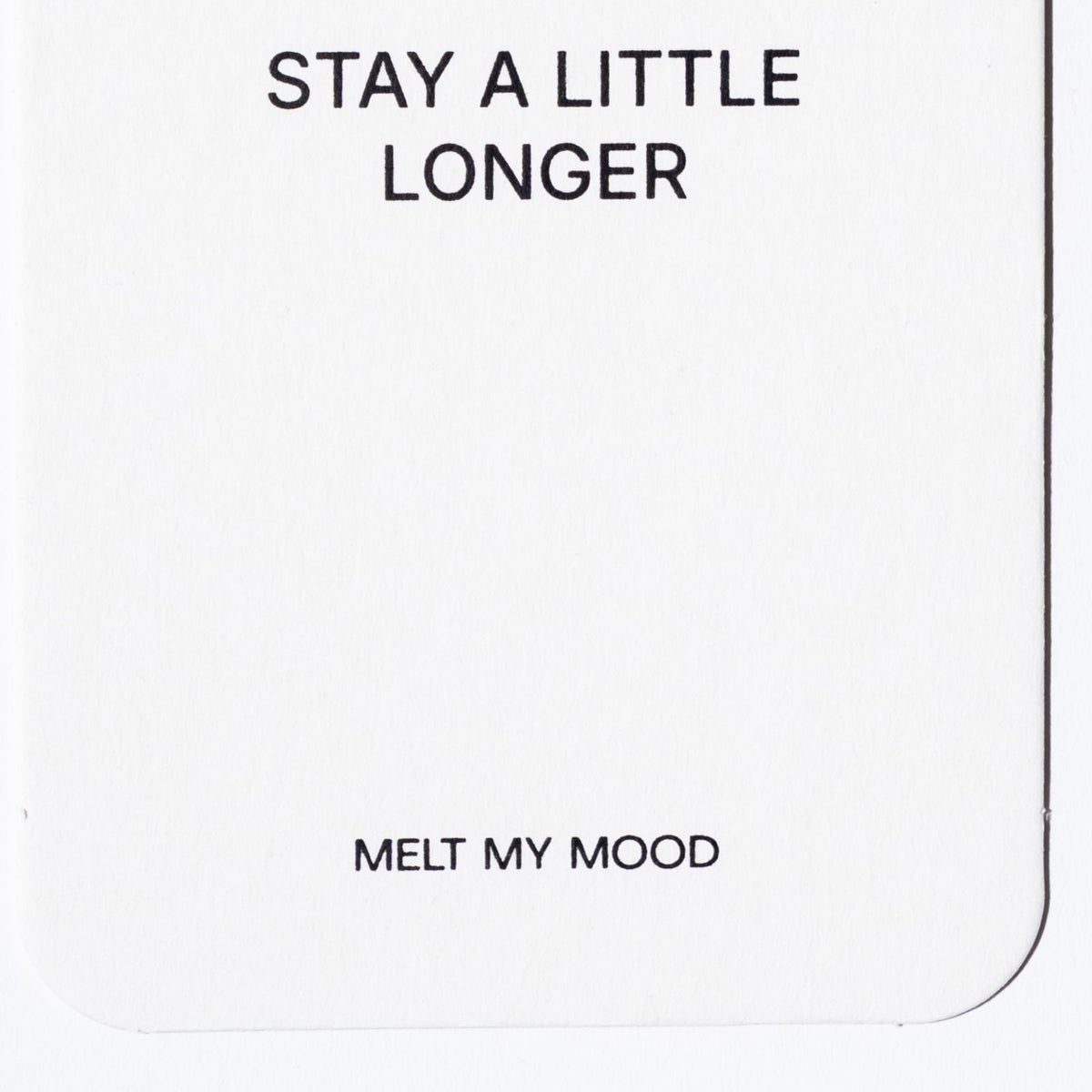 Közelkép egy lekerekített sarkú, fehér, téglalap alakú gardróbillatosítóról, amelynek felső részén a „STAY A LITTLE LONGER”, alsó részén pedig a „MELT MY MOOD” felirat látható fekete betűkkel.